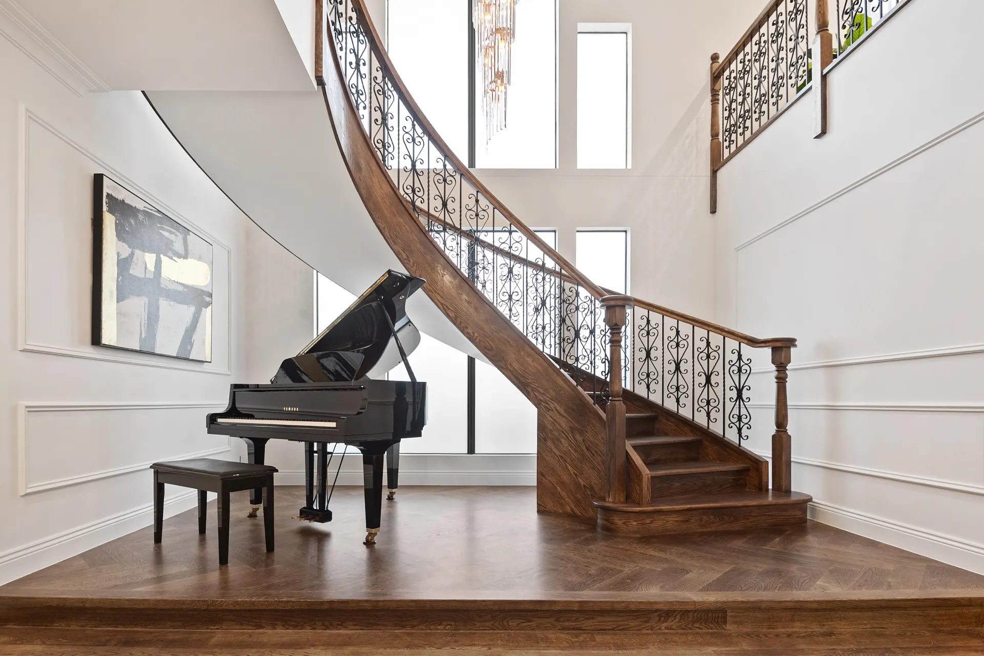 Curved timber staircase with a wrought-iron balustrade rising from an engineered oak herringbone entry